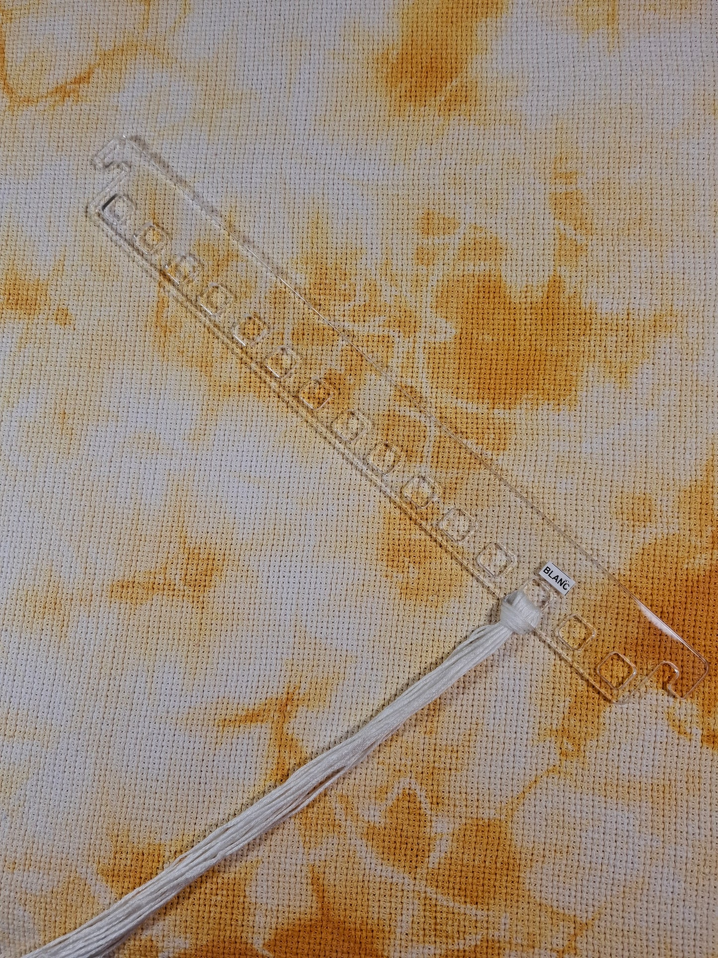 Colgador de hilos acrílico transparente sobre fondo texturizado, mostrando espacio para organizar 15 colores de hilos.