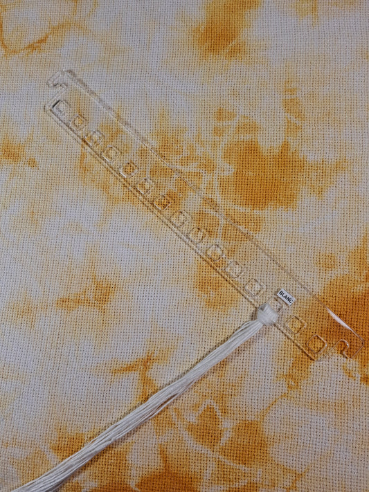 Colgador de hilos acrílico transparente sobre fondo texturizado, mostrando espacio para organizar 15 colores de hilos.